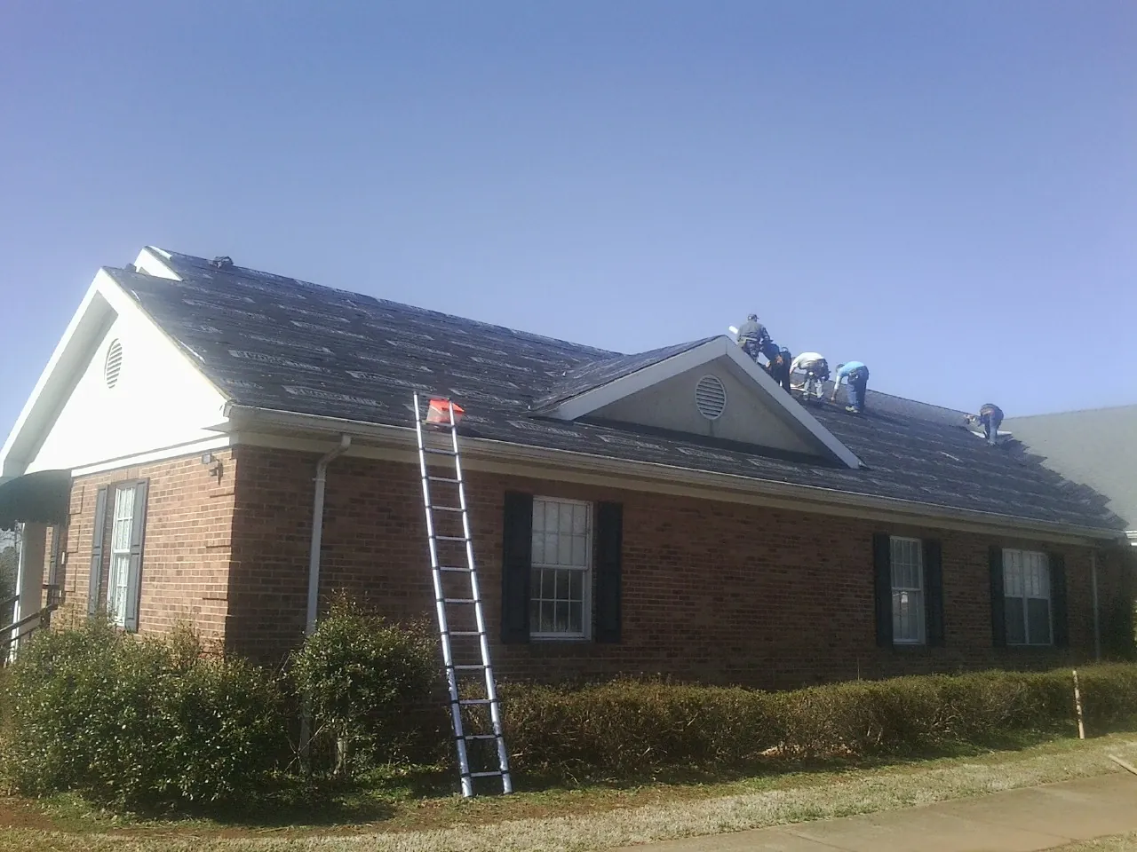 Crew tearing shingles off a brick ranch roof with a ladder set — Metal Roof Repair work by our crew in Elk Point