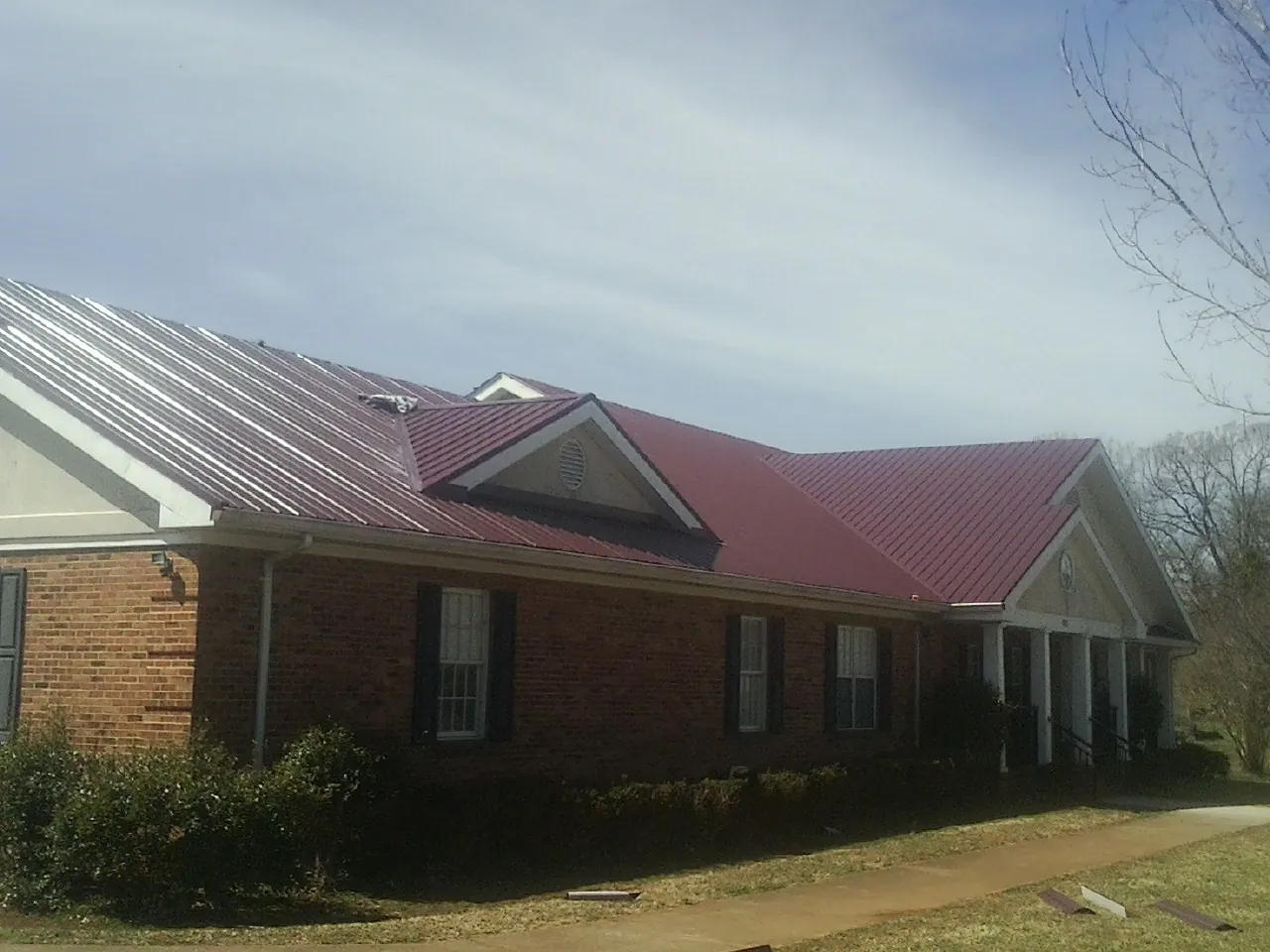 Red metal roof with gabled entries on a long brick building, from a Hail Damage Roof Repair job in Elk Point
