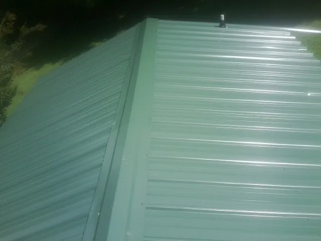 New green metal panels meeting at the ridge of a roof — Flat Roof Repair work by our crew in Elk Point