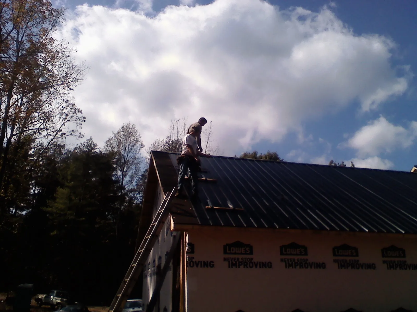 Roofer fastening dark metal panels high against a cloudy sky, from a Roof Inspection job in Elk Point